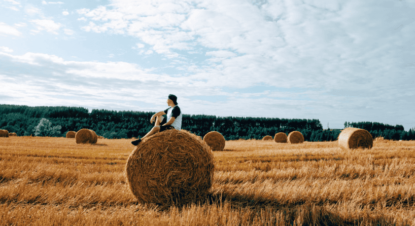 Man sitting on hay bale in field, looking out into the horizon.